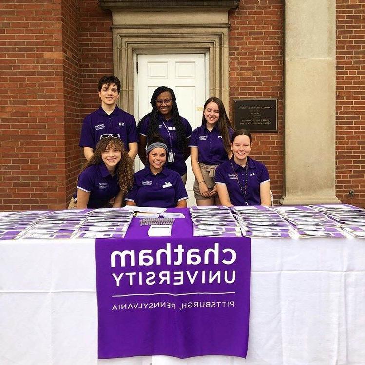 Photo of six Chatham University students in purple shirts, working at a table outside on 足球外围盘官方网站